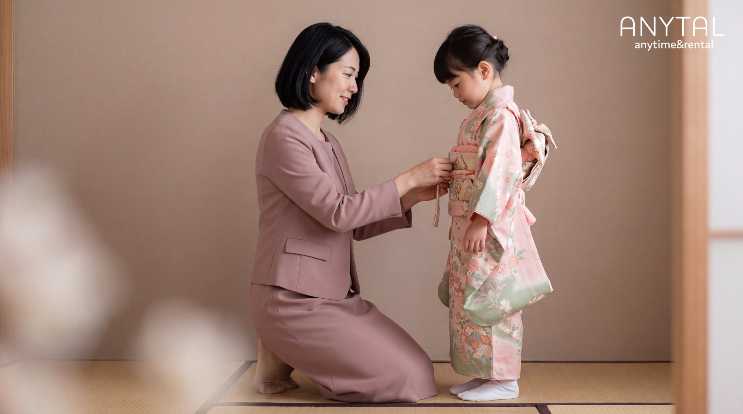 落ち着いたピンクのスーツを着た母親が、七五三の晴れ着を着た子どもの帯を整える様子