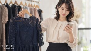 ネイビーのドレスをハンガーに掛けて持ちながら、スマートフォンで利用方法を確かめる20代の女性
